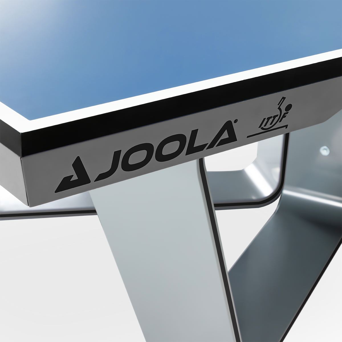 Tischtennisplatte JOOLA mit blauem Spielfeld und weißem Gestell, Detailansicht der Kante mit Logo.